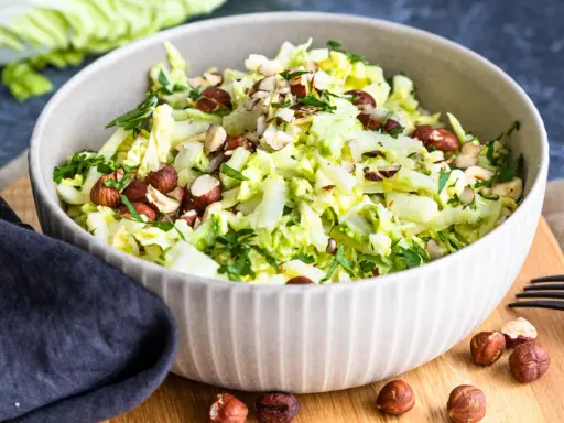 Frischer Chinakohlsalat mit gehackten Haselnüssen und Petersilie, serviert in einer Schüssel.
