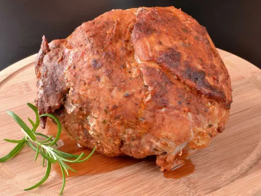 Pieczona szynka z ziołami, która wygląda jakby była przygotowana z użyciem marynaty do szynki. Gałązka rozmarynu dodaje aromatu.
