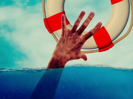 Dłoń wyciągnięta z wody chwyta koło ratunkowe. To symbol nadziei i szansy na nowe życie, jak w przypadku wczasów odwykowych dla alkoholików.
