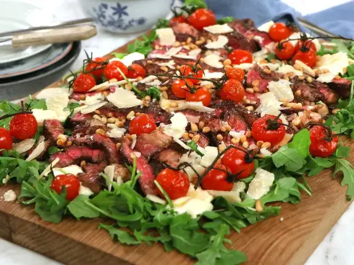 En läcker biff tagliata med körsbärstomater, pinjenötter och parmesan på en bädd av rucola.