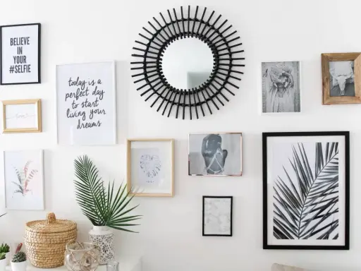 Un mur de cadres éclectique avec un miroir soleil, des photos et des citations inspirantes.