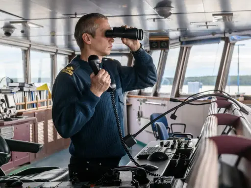 Un officier de marine, comment s'appelle la personne qui conduit un bateau, utilise des jumelles et un téléphone dans la passerelle.