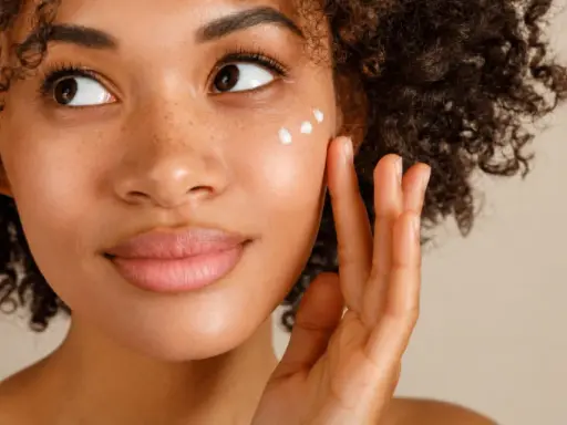 Donna con capelli ricci applica crema sul viso per una pelle bella e luminosa.