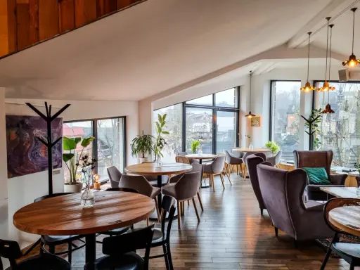Przytulna restauracja w Bukowinie Tatrzańskiej z widokiem na góry. Drewniane stoły, wygodne fotele i stylowe oświetlenie tworzą ciepłą atmosferę.