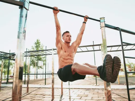 Uomo muscoloso esegue un esercizio di calisthenics per principianti alla sbarra, sollevando le gambe.