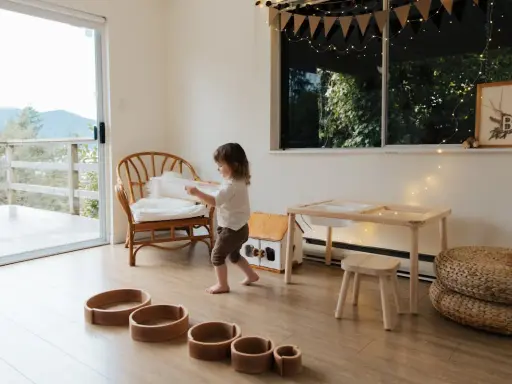 Bambina gioca in una stanza giochi in casa, tra sedie di vimini, tavolino e cesti.
