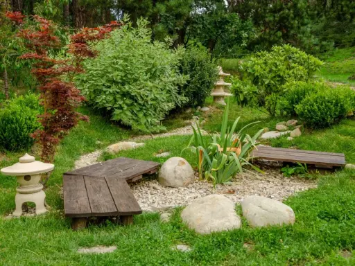 Un paisible petit jardin japonais avec des lanternes, des bancs en bois, des rochers et une végétation luxuriante.