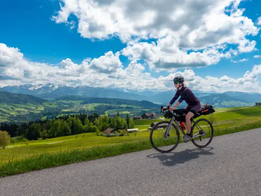 Frau fährt mit Bikepacking-Ausrüstung auf einer Straße mit Alpenpanorama.