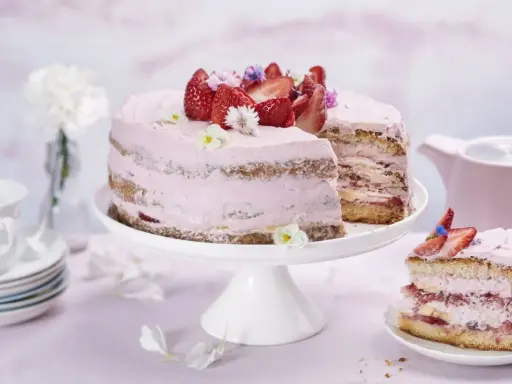 En vacker jordgubbstårta med rosa frosting och färska jordgubbar. En bit är uppskuren och ligger på en separat tallrik.