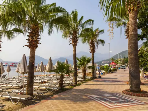 Alejka z palmami prowadzi do plaży w Marmaris, Turcja. Leżaki i parasole czekają na turystów.