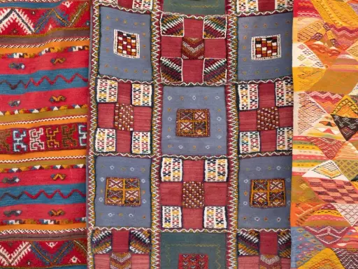 Bunte Teppiche mit geometrischen Mustern, die das orientalische Flair widerspiegeln. Ein Teppich zeigt Streifen, ein anderer Quadrate und das dritte Rauten.