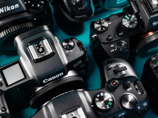 Zbliżenie na kilka nowoczesnych bezlusterkowców marek Nikon, Canon i Sony, ułożonych na turkusowym tle.