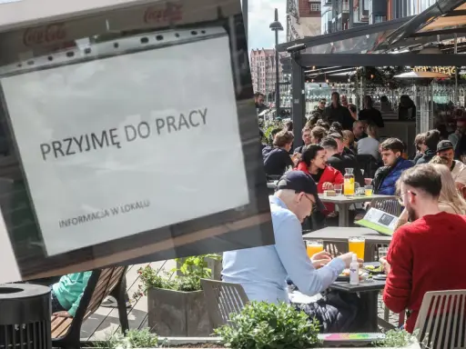 Ogłoszenie "Przyjmę do pracy" na tle ogródka restauracyjnego z ludźmi przy stolikach.