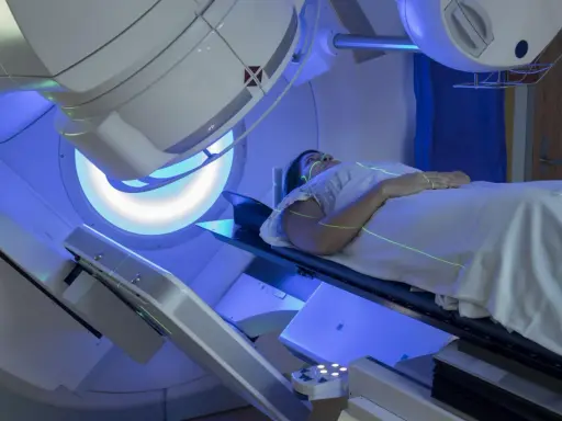 Pacjentka leży na stole terapeutycznym pod aparatem do radioterapii. Zielone linie laserowe wyznaczają pole napromieniania. To właśnie radioterapia co to jest – nowoczesna metoda leczenia.