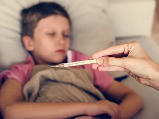 Dziecko z gorączką, czuć zimne rączki i nóżki. Mama mierzy temperaturę termometrem.