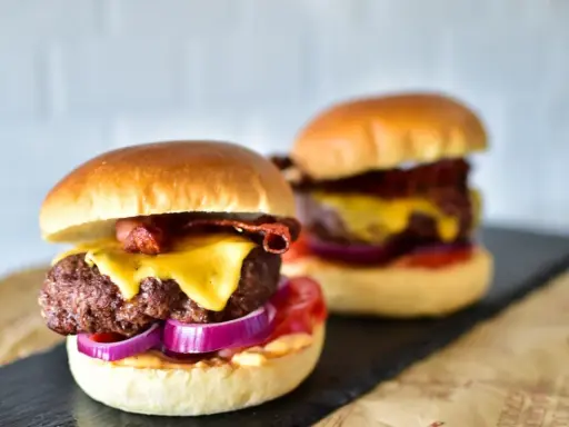 Zwei saftige Burger im Airfryer zubereitet, mit geschmolzenem Käse, knusprigem Speck und roten Zwiebeln.