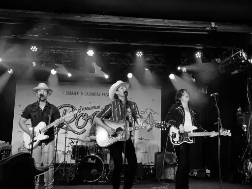 Band spelar på scen i Stockholm, med cowboyhattar och gitarrer. Kanske en hyllning till Fleetwood Mac Stockholm?