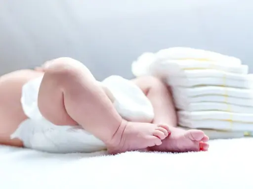 Nietolerancja laktozy u niemowlaka? Śluz w kupie może być sygnałem. Na zdjęciu nóżki dziecka i stos pieluch.