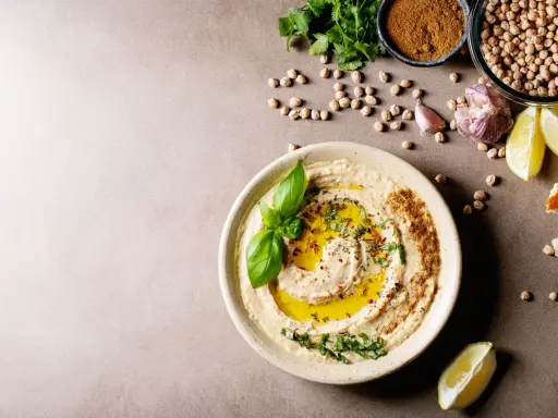 Pyszny hummus z oliwą, ziołami i bazylią. Obok ciecierzyca, czosnek, cytryna i chleb. Czy można mrozić hummus? Tak, można go mrozić.