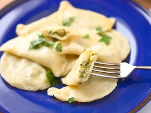Pyszne pierogi ze szpinakiem, polane masłem i posypane natką pietruszki, czekają na widelcu.