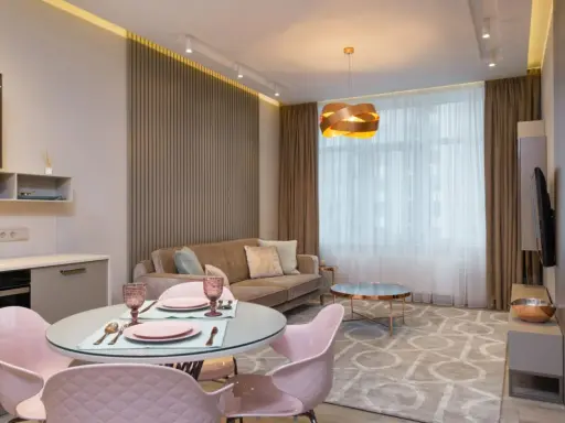 Nowoczesny salon z aneksem kuchennym po generalnym remoncie mieszkania 50m2. Jasne kolory, welurowa sofa i różowe krzesła tworzą przytulną atmosferę.