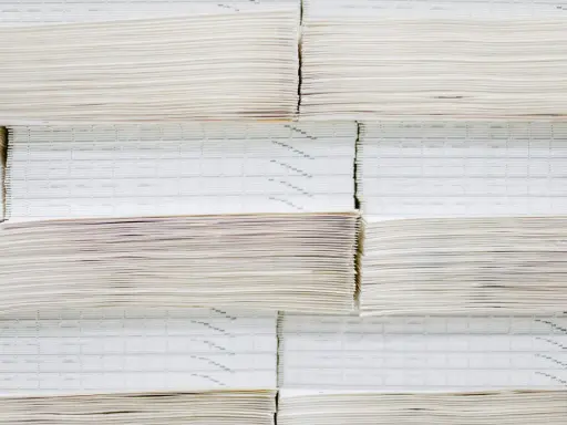 Grandes pilas de papel offset, algunas con finas líneas impresas, apiladas ordenadamente en un almacén.
