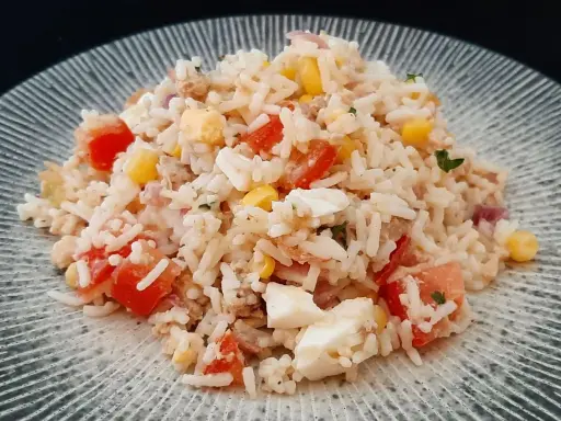 Salade de riz, thon, tomates, maïs et œuf dur sur une assiette grise.