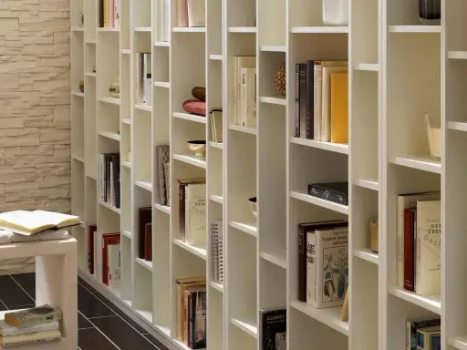 Eine weiße, modulare Bücherwand, perfekt für dein Projekt "Bibliothek selber bauen". Viele Bücher und Deko-Objekte sind ordentlich einsortiert.