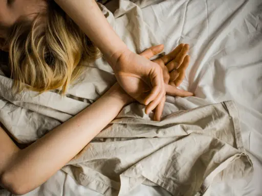 Blonde Haare auf einem Kissen, Arme schlafen nachts ein, Hände ruhen auf der Decke.