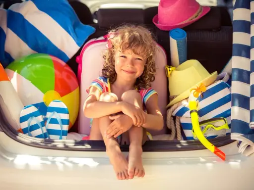 Niña sonriente rodeada de artículos de playa, lista para explorar nuevos sitios para ir con niños.