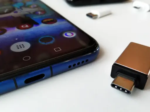 Złoty adapter USB-C i białe przejściówki leżą obok niebieskiego smartfona. Dowiedz się, jak podłączyć pendrive do telefonu.