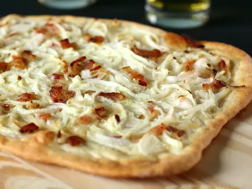Flammekueche généreuse garnie d'oignons crus ou cuits et de lardons croustillants, prête à être dégustée.