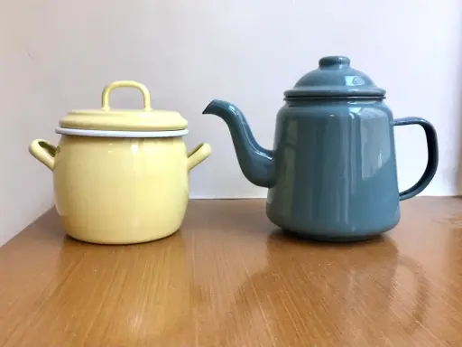 En gul gryta och en blå kaffepanna i emalj, liknande en klassisk kockums kaffepanna, står på ett träbord.