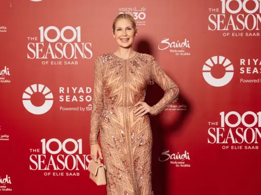 A woman in a sparkling celio saab gown poses at an event with "1001 Seasons of Elie Saab" branding.