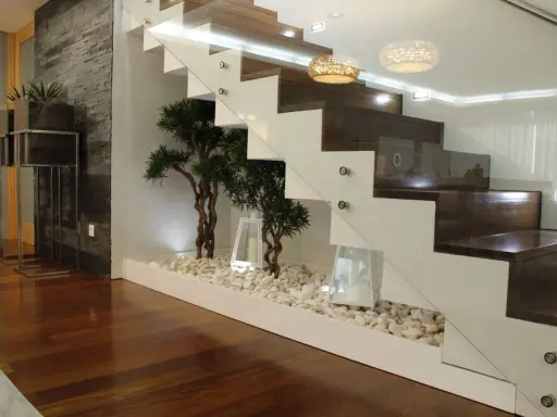 Elegante subida de escalera interior con plantas decorativas y piedras blancas.