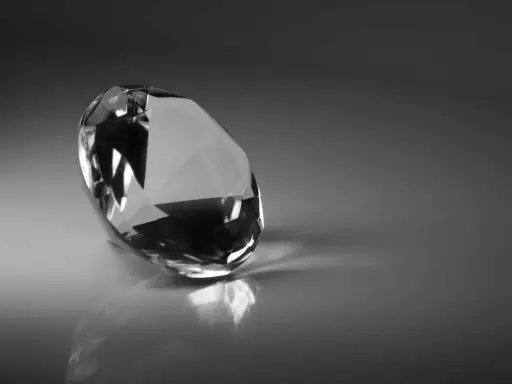 Un diamante sfaccettato riflette la luce su una superficie lucida. Il suo fascino misterioso evoca il significato dei diamanti neri: forza e resilienza.