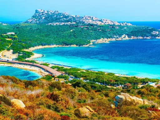 Vacker kustlinje med turkost vatten, en bro och gröna kullar. En dröm för en **Sardinien resa**.