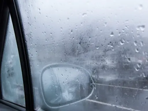 Gotas de lluvia en el cristal del coche, reflejando el exterior y el espejo retrovisor. Una escena que explica porque se empañan los cristales en días húmedos.