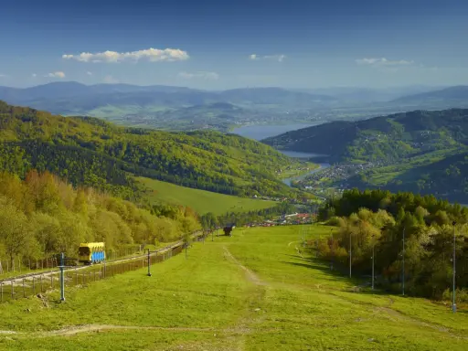 Widok na zielone beskid mały szczyty, jezioro i miasteczko. Kolejka krzesełkowa wjeżdża na górę.