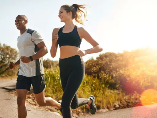 Ein Mann und eine Frau joggen lachend auf einem Feldweg. Die Sonne scheint, und die Atmung beim Joggen ist gleichmäßig und tief.