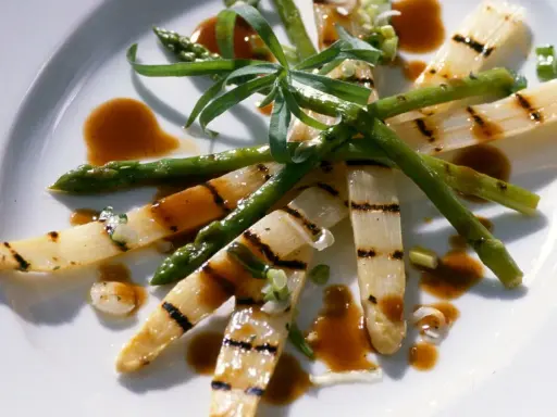 Gegrillter Spargel auf einem Teller, mit einer würzigen Sauce beträufelt und garniert mit frischen Kräutern.