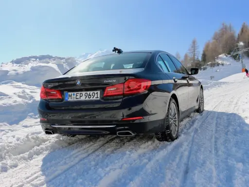 Schwarzer BMW 540i G30 fährt durch tiefen Schnee auf einer Skipiste, bergauf mit Skilift im Hintergrund.