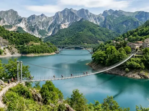Un ponte sospeso attraversa il lago di Vagli, con montagne imponenti e un borgo pittoresco sullo sfondo.