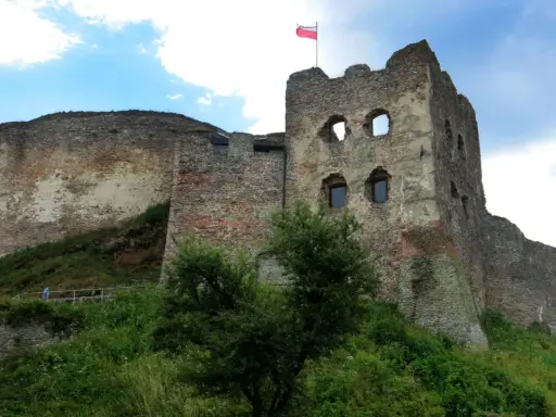 Ruiny zamku Czorsztyn na wzgórzu, z polską flagą powiewającą na wieży.