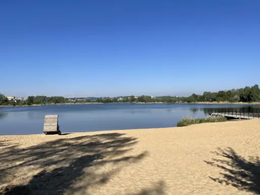 Plaża bagry z drewnianą przebieralnią i pomostem, w tle jezioro i zieleń.