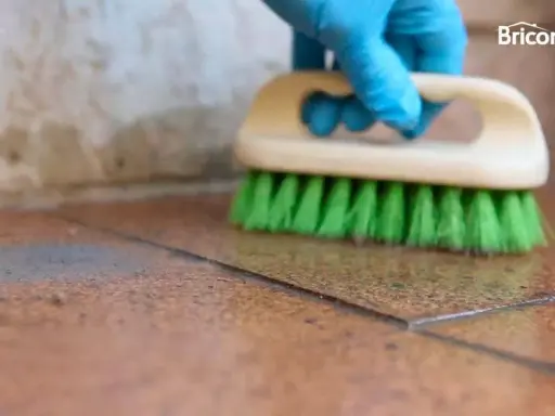 Guante azul cepilla suelo de baldosas para quitar cemento cola.