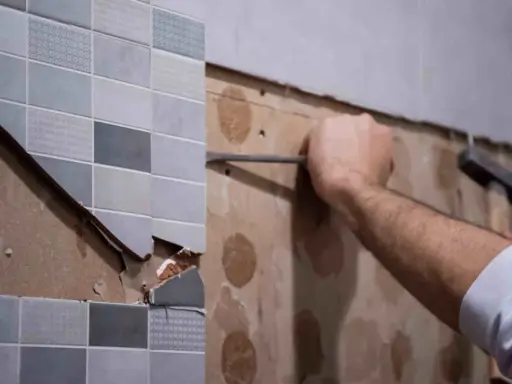 Persona usando una espátula para quitar azulejos de una pared.