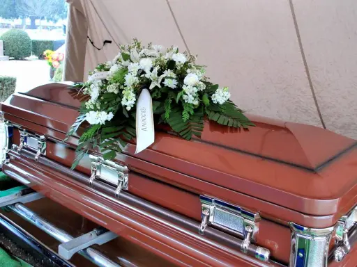 Brązowa trumna z wieńcem białych kwiatów. Na wstędze widnieje napis "GRANNY". Informacje, jak sprawdzić datę pogrzebu, można znaleźć w nekrologach.