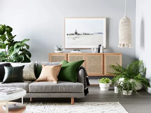 Accogliente zona giorno con divano grigio, cuscini colorati, credenza in rattan e piante verdi.