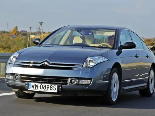 Elegancki Citroën C6 w kolorze granatowym jedzie po drodze. Wnętrze z jasną tapicerką i kierowcą.